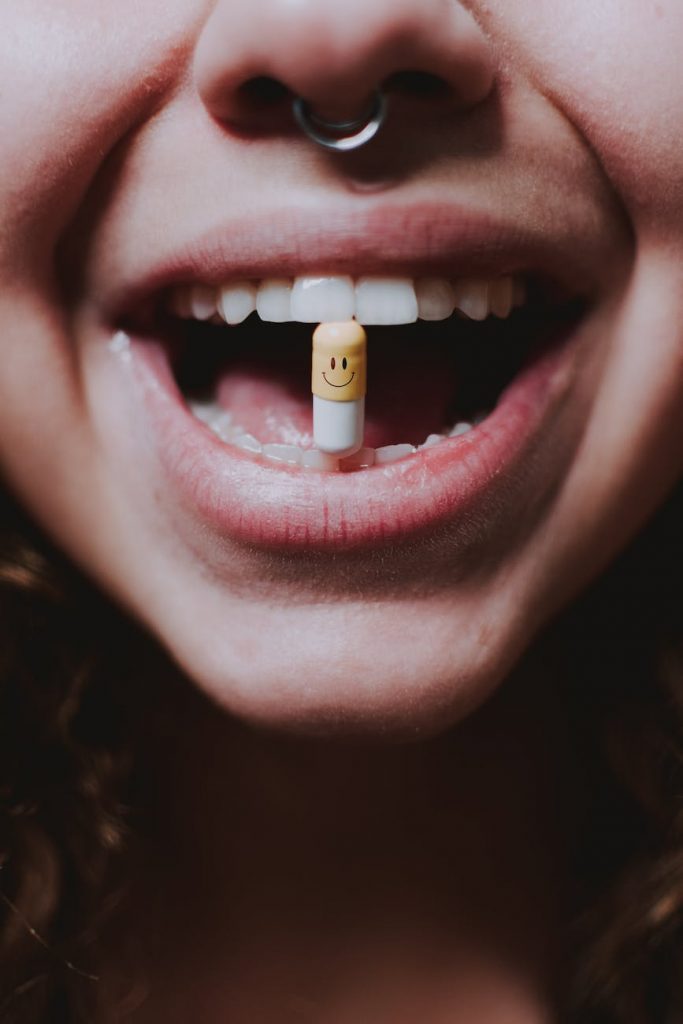 faceless woman with pill in teeth and nose piercing